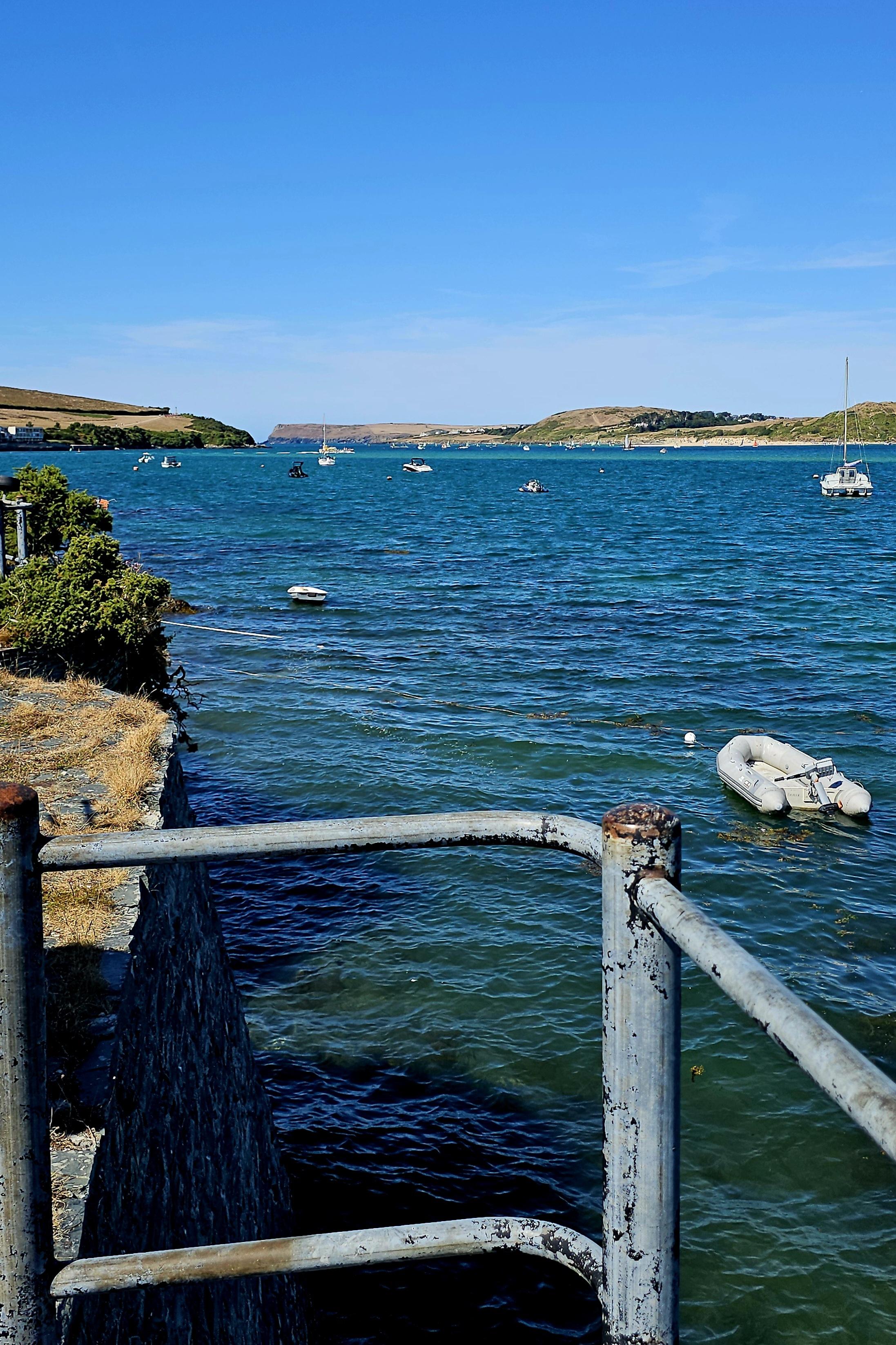 View over a railing, across a blue estuary dotted with small boats.