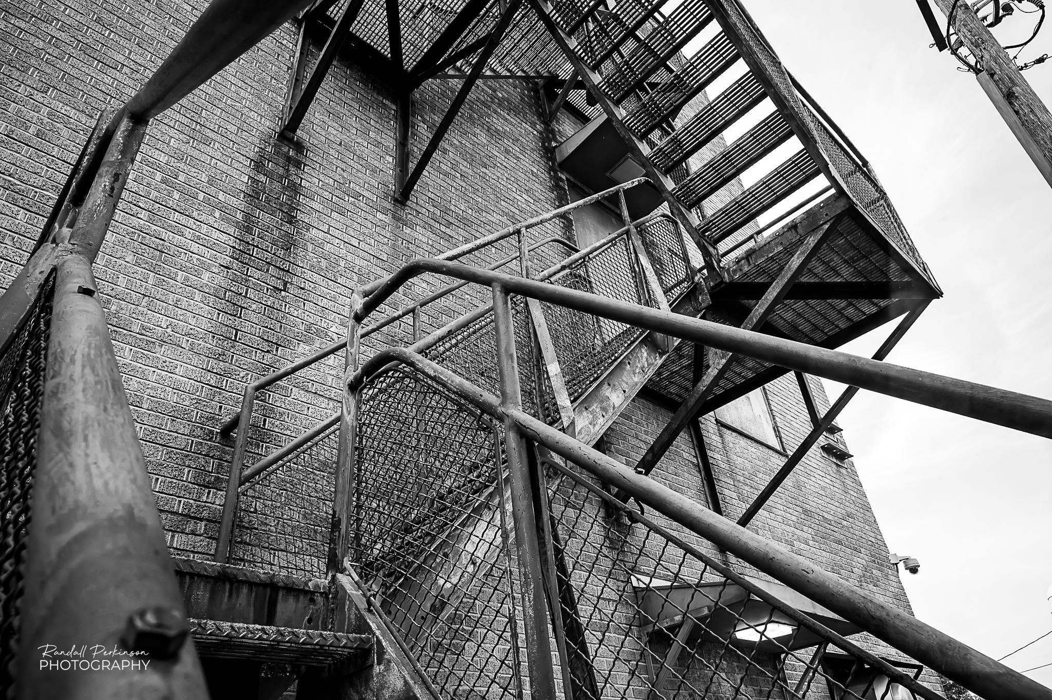 Looking up at metal fire escape stairs on the side of a brick building.