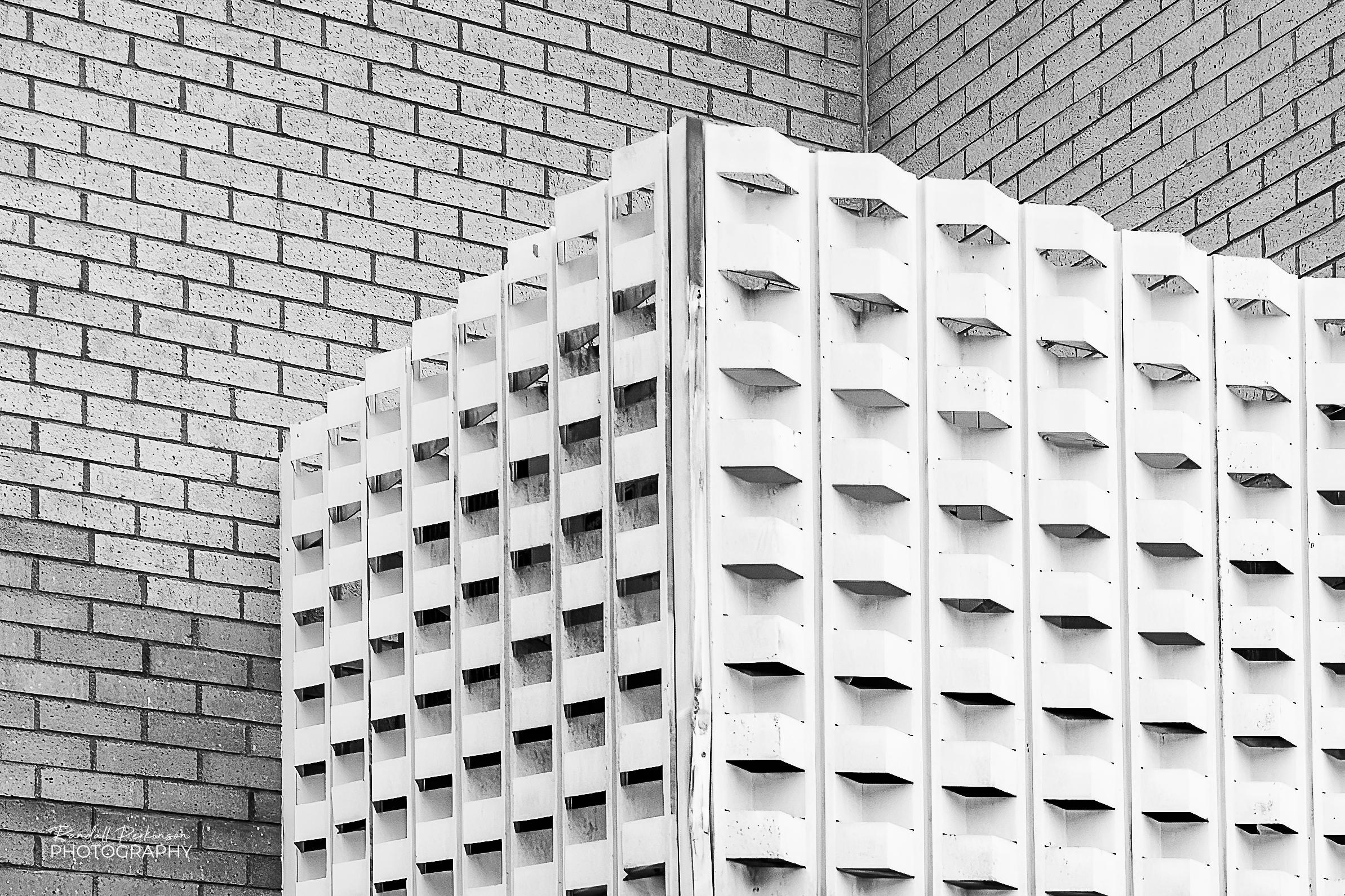 A mid-century modern metal 3D panel hides an area above an entrance to a brick bank building.