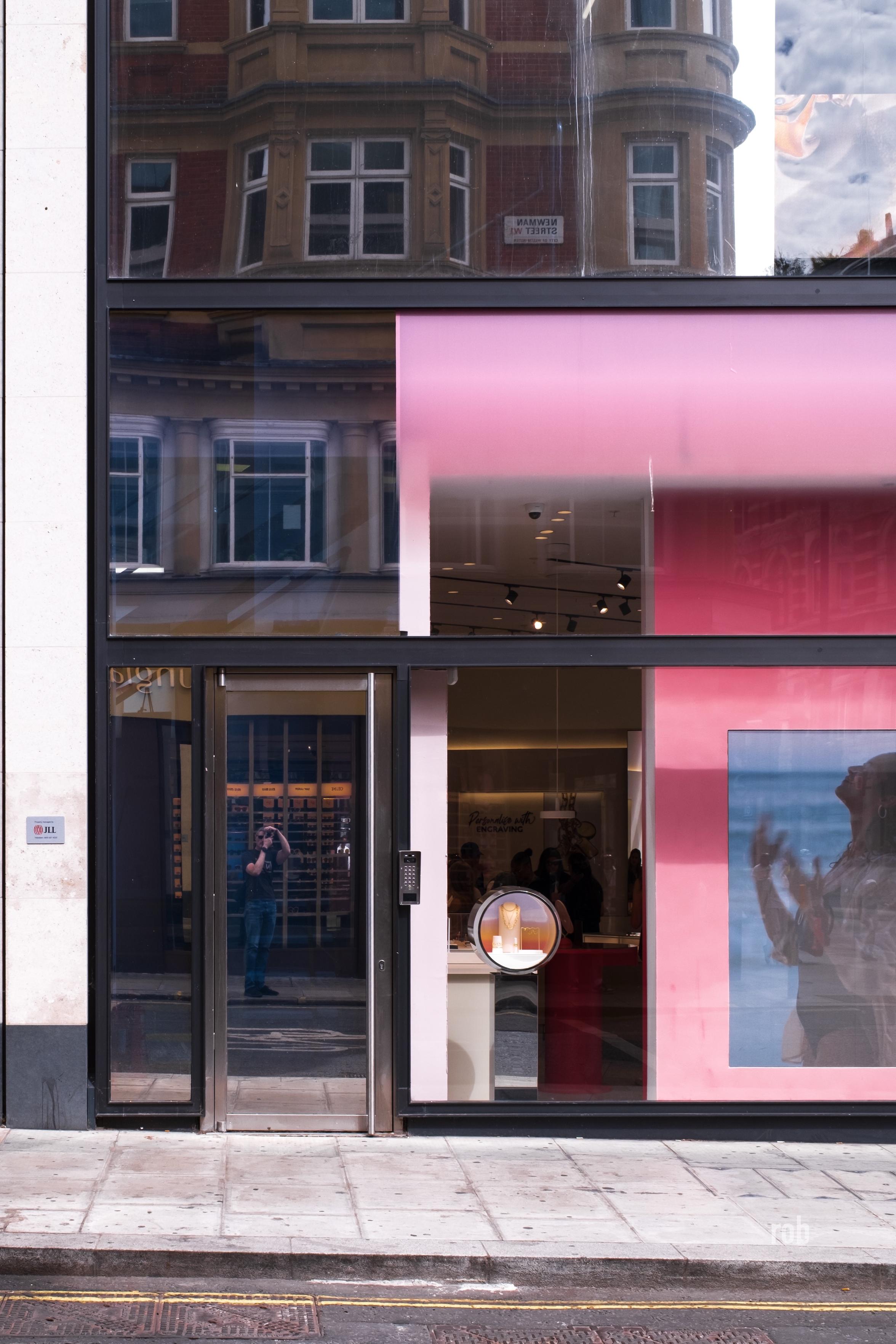 A flat straight on shot of a glass modern building, the shot is just tight enough and the inside of the building dark enough that the reflection of the building opposite might be mistaken as not a reflection. A large section of a pink coloured non-reflective storefront on the bottom right quarter of the scene gives it away though. Also the reflection of the photographer, that too.