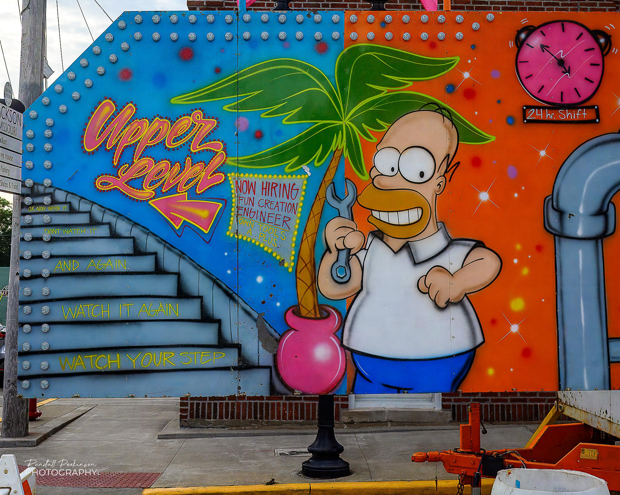 The side of a carnival trailer showing Bart Simpson holding a wrench, a palm tree in a pink pot.