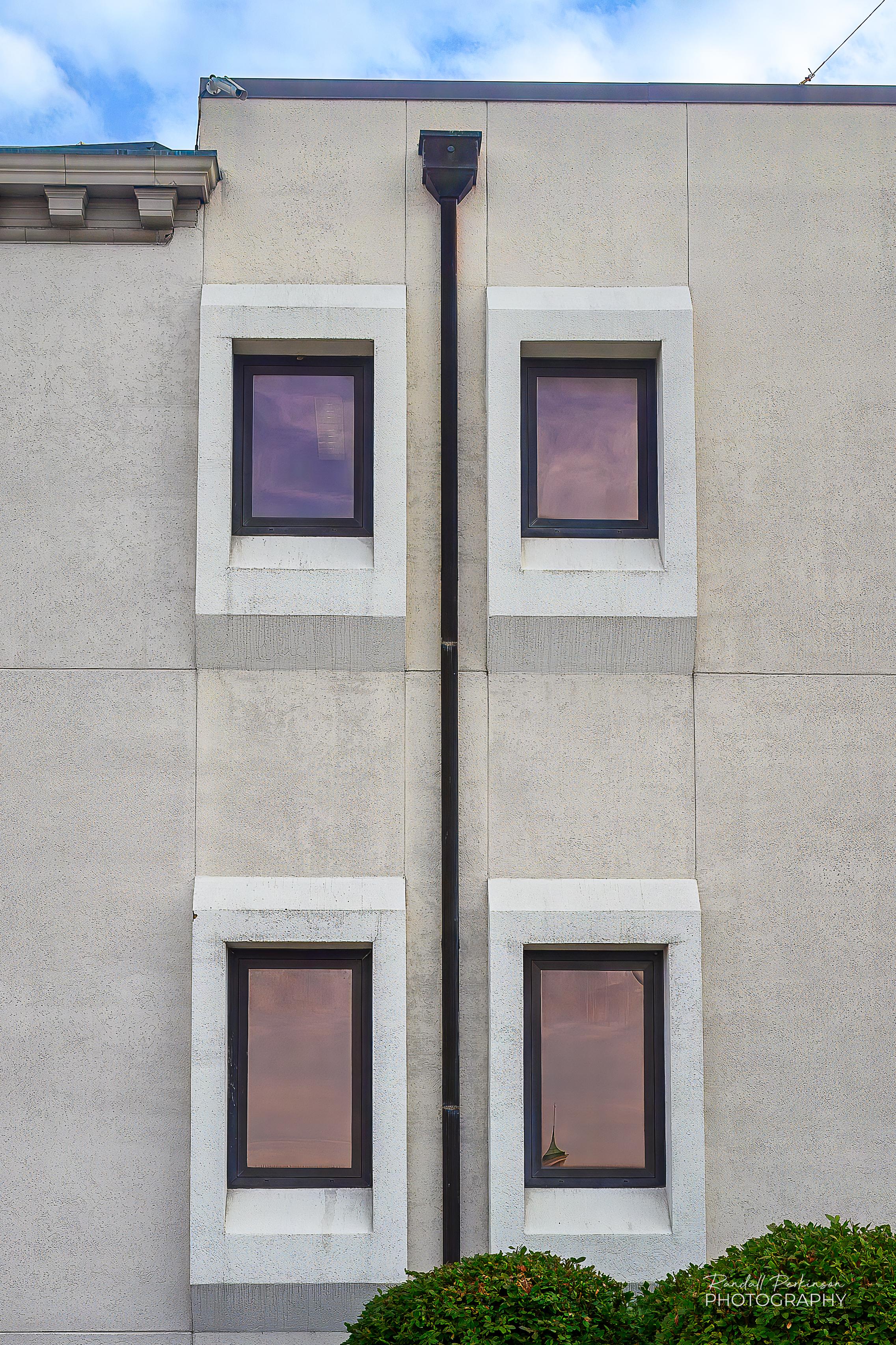 A view of the side of a building with four windows and a downspout bisecting them.