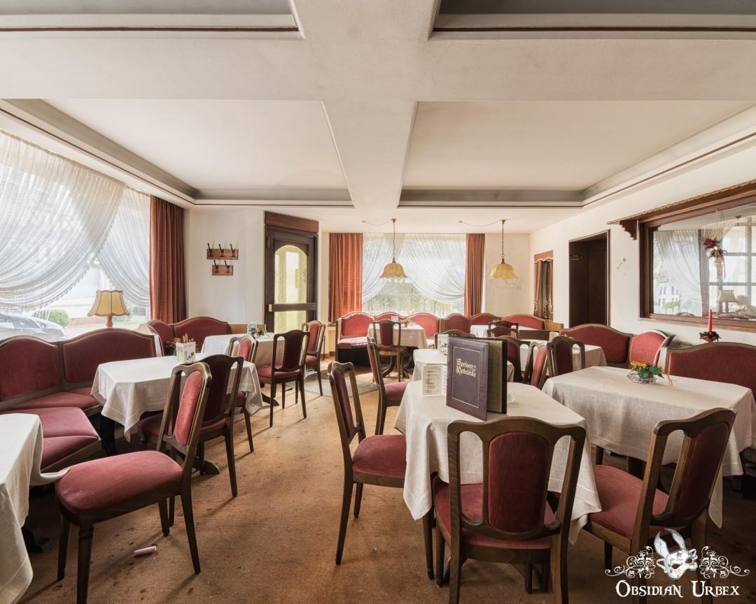 An empty restaurant features red chairs, white-clothed tables, and large windows.