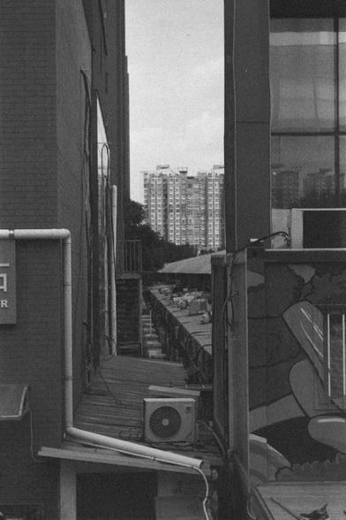 Ilford HP5 Plus 400 (FF)

English
A black and white photograph of a group of buildings. Some have AC outdoor units on the condense pad. The picture is taken through between two buildings. Another high-rise can be seen in the back.

中文
一張黑白照片.照片中有一組樓房.樓房外有空調的外機. 照片的角度是透過兩棟房子之間的空間拍攝.遠處可以看見另一棟高樓.