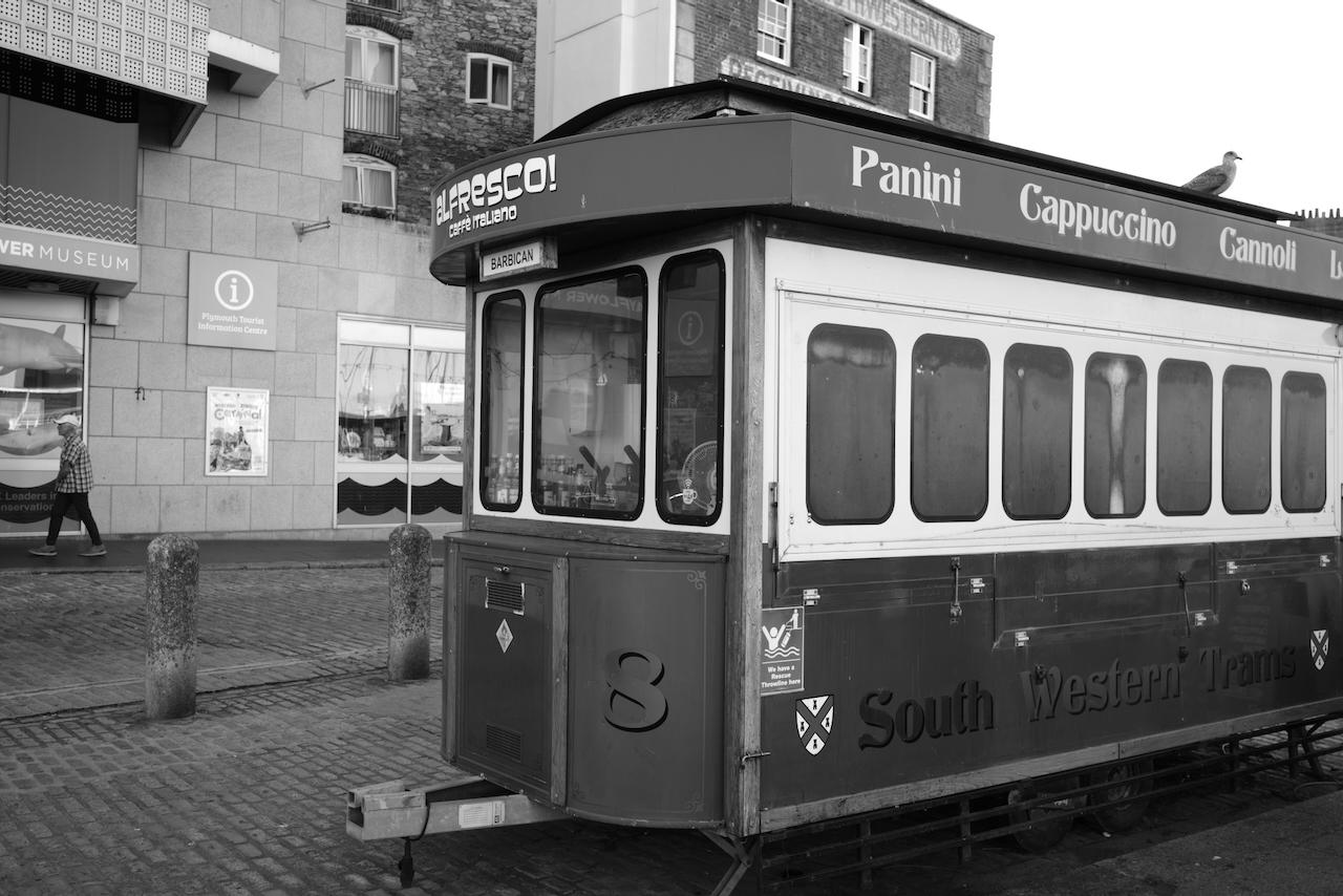 A black and white photo of an trailer styled to look like a 1930's tram/trolly. There's a seagull sitting on top of it.