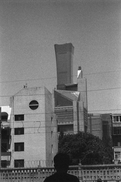 Ilford HP5 Plus 400 (FF)

English
A black and white photograph of an urban skyline. One skyscraper stands out amongst a group of high-rises. A person’s silhouette can be seen in front of the buildings. Some trees stand in front of one of the building. The sky is bright with gradience.

中文
一張城市天際線的黑白照片.一座摩天大樓在一群高樓中脫穎而出.一個人的輪廓在前景中清晰可見.一棟樓前有一顆樹.天空明亮有層次.