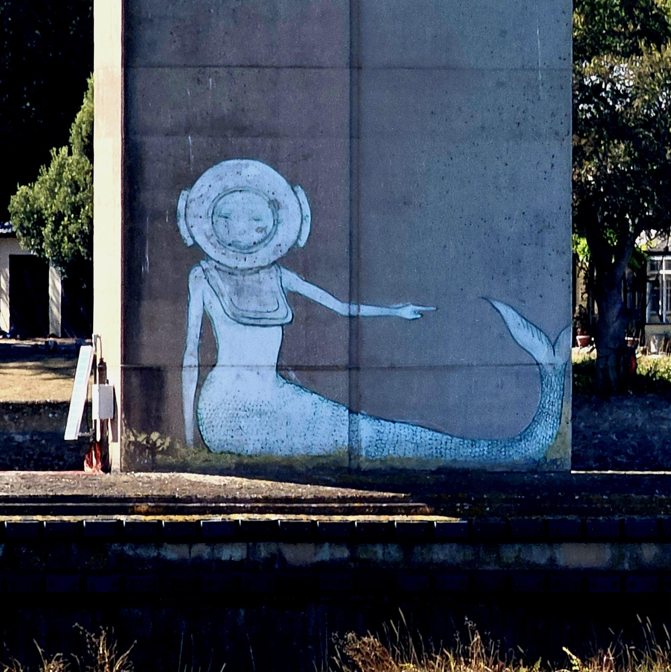 Large drawing of a mermaid in a diving helmet on a concrete bridge support.