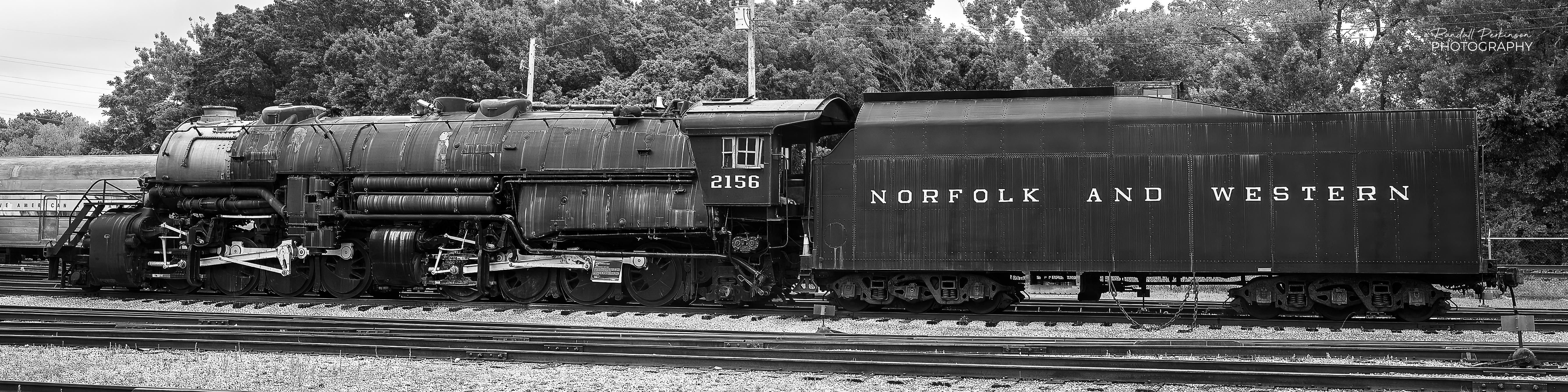 A wide picture showing the entirety of the Norfolk and Western Railway No. 2156 steam locomotive and it's tender.  The Class Y6a 2-8-8-2 steam locomotive was building in Roanoke, Virginia.  It is the last surviving member of the Y6a class and has been at the National Museum of Transportation since 1959.  It is regarded as one of the most efficient and powerful heavy freight steam locomotive designs ever built.