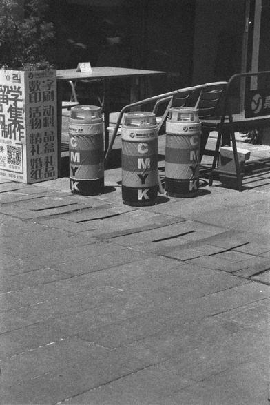 Ilford HP5 Plus 400 (FF)

English
A black and white photograph of three columns on the ground featuring the letter C M Y K on each of them. The columns stand in front of a group of chairs and by the side of a pot of greens. It seems to be an art piece in public space.

中文
一幅黑白照片.照片中有三個立柱,每個都寫著CMYK的英文字母.立柱後面有一些椅子,旁邊還有種植著植物的花壇.這些立柱似乎是某公共空間的藝術創作.