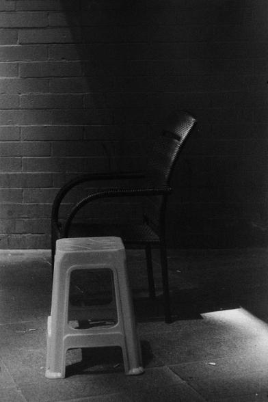 ERA 100 (FF)

English
A black and white photograph of a plastic stool and a wooden chair. The stool and the chair are in the shadow at a corner in front of a brick wall. The light is dim.

中文
一張黑白照片.照片中有一張塑料板凳和一張藤椅在角落的陰影中.角落在一面磚牆的前面.光線昏暗.