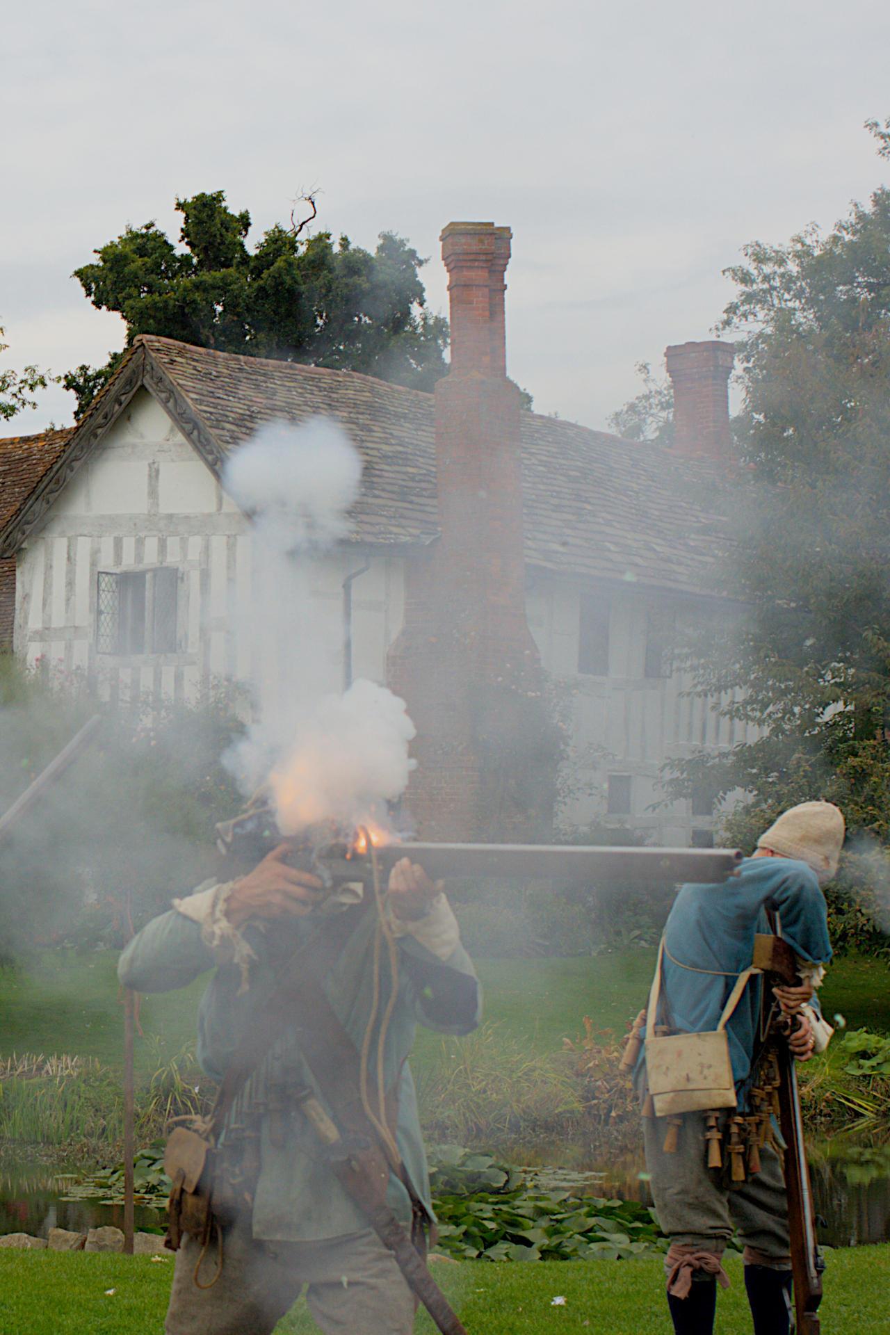 English Civil War reënactor firing a matchlock musket, the man's face is obscured by smoke, there is flame from where the smouldering match has ignited the gunpowder primer, literally a flash in the pan.

A second reënactor is loading his musket. Behind both is the 14ᵗʰ century Lower Brockhampton House.


Canon EOS 400D DIGITAL
ISO: 200
Shutter Speed: 1/320
Aperture: 6.3

Lens: 35.0 mm
Focal Length: 35.0 mm (35 mm equivalent: 56.6 mm)
Hyperfocal Distance: 10.47 m
Field Of View: 35.3 deg

GPS position: 52 deg 12' 03.7" N, 2 deg 27' 30.2" W
Lower Brockhampton, Bromyard, Herefordshire, UK

2007:09:30 14:55:49
Copyright: © Matthew Malthouse 2007