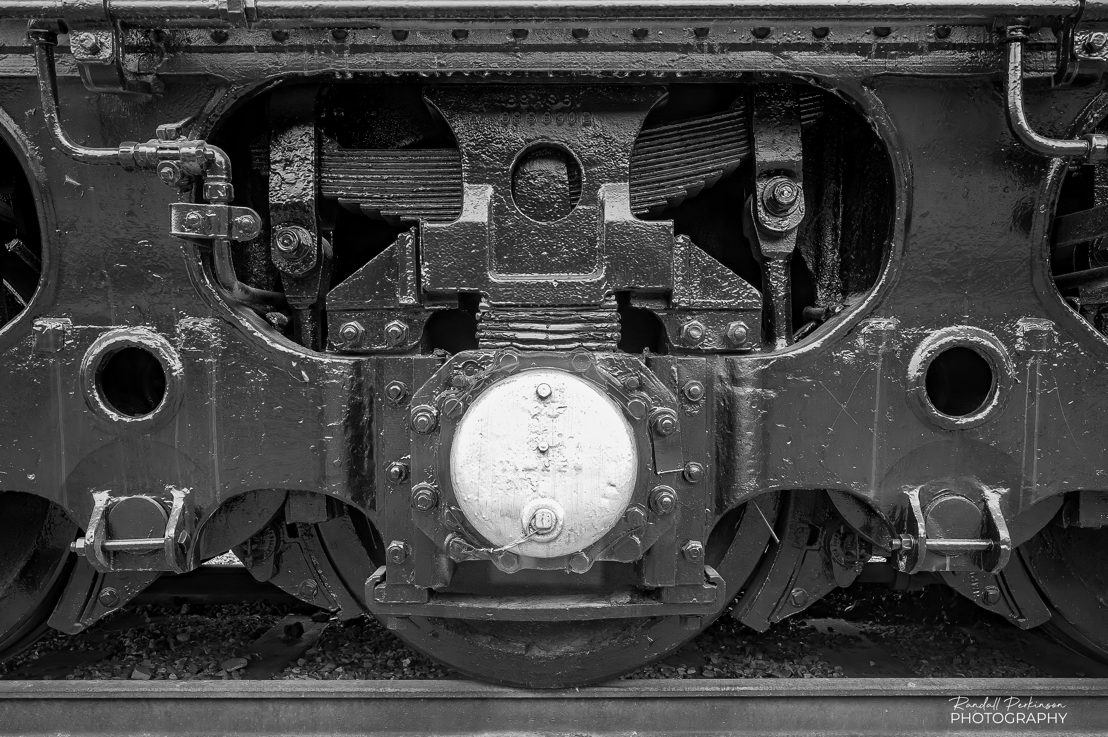 A black and white image of the undercarriage of a locomotive showing wheels, bearings, brakes, and springs.