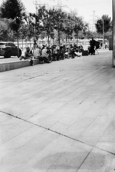 ERA 100 (FF)

English
A black and white photograph of a street scene. A group of people sitting in the background in front of some trees planted on the side of the road where some cars are parked. The foreground is empty. Only the tiled road can be seen.

中文
一张街景的黑白照片.一群人坐在街边.街边种着树,还停靠着一些汽车.前景空旷,只能看到地砖.