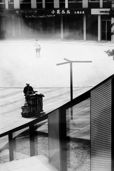 ERA 100 (FF)

English
A black and white photograph of a public square. A person stands in the center while a member of the cleaning crew is cleaning the ground. Stairs are in the foreground making an intriguing shape. The square is surrounded by a couple of shops.

中文
一张广场的黑白照片.广场中央站了一个行人.前景中有一个人正在清扫地面.前面是一个阶梯,形成了有趣的构图.广场被一些商店包围.