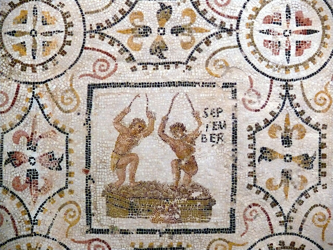 Color image of a third century BCE Roman mosaic with two men crushing grapes on the September panel of the months at El Djem, Tunisia - then Roman Africa - the vintage is a characteristic activity of the month in Roman art.  Image shows two men crushing grapes with their feet, the word SEPTEMBER written in tile in the upper left, the image surrounded by decorative tiles. First half third century BCE,  conserved by the Archeological Museum of Sousse, Netherlands.
