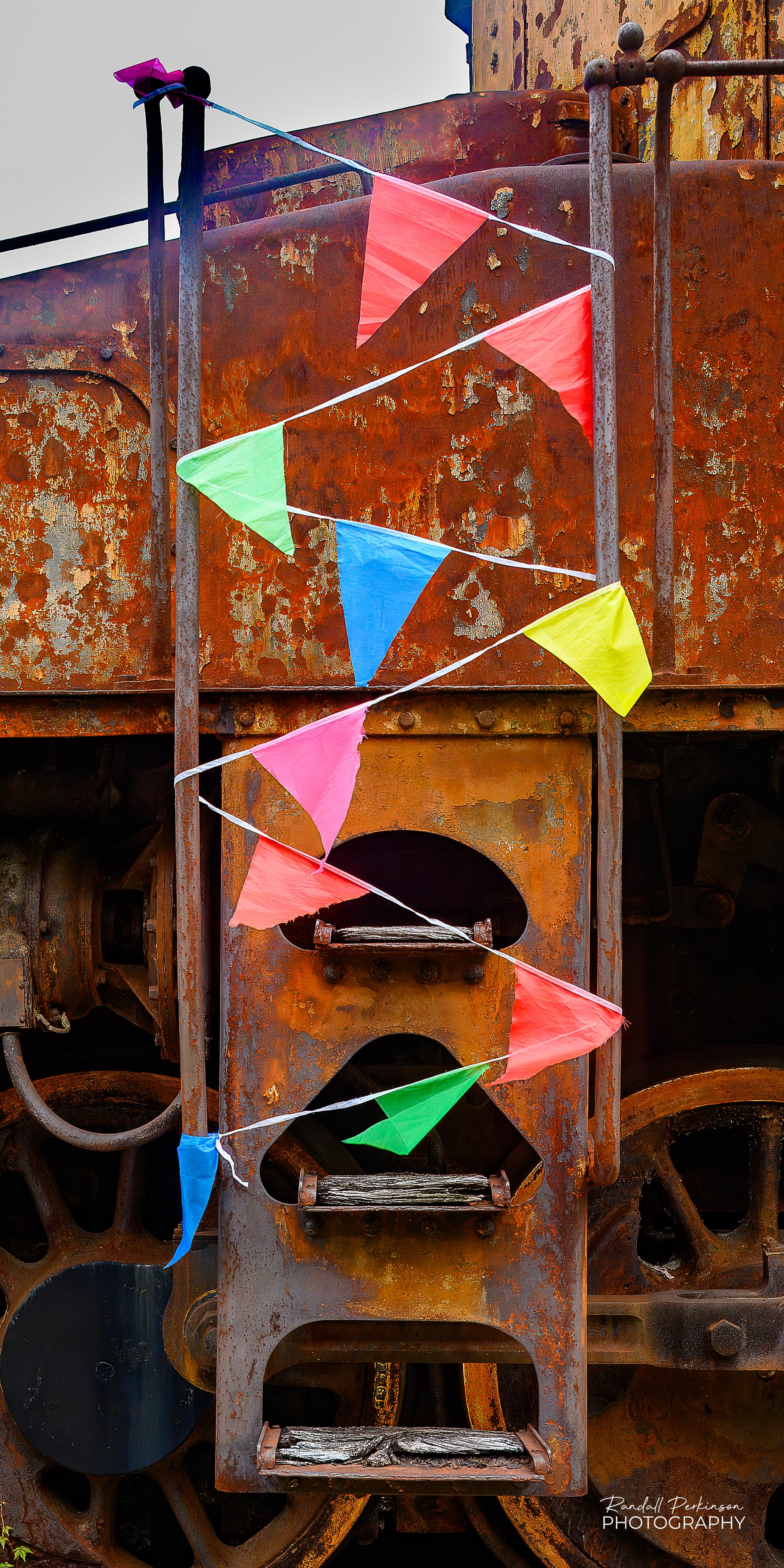 A ladder up the side of an old, very rusty, steam locomotive has a string with brightly colored triangular flags along it wrapped back and forth around a ladder to discourage anyone from climbing on it.