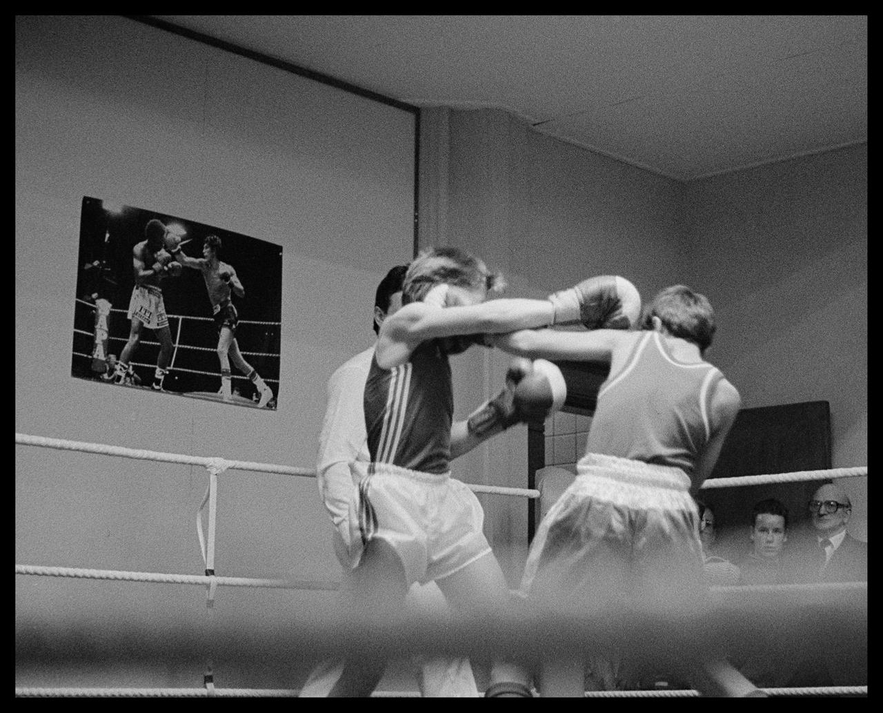 B&W photograph taken sometime in the mid 1980s.

Two young boxers fighting in a boxing ring at the local amateur boxing club. Some spectators are seen on the right, boxers are in the middle of the frame and on the top left a poster of an ongoing boxing match can be seen.

Fortunately, you don’t see this sort of thing any longer at any self-respecting boxing club; No head protection. If I remember correctly, these lads were about 12 or 13 years old.

Camera: Nikon F801s
Lens: Nikkor AF 50mm f/1.8D
Film: Ilford HP5 (@800)