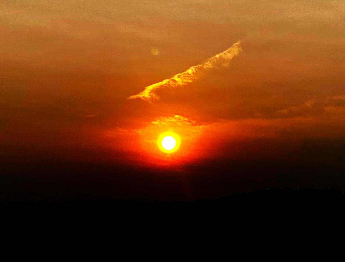 Color image of sunset, Atwood Lake, Tuscarawas County, Ohio, USA. Image shows the sun's orange sphere dropping to the horizon, a wispy cloud above illuminated, sky orange to green to blue, black hillsides below.
