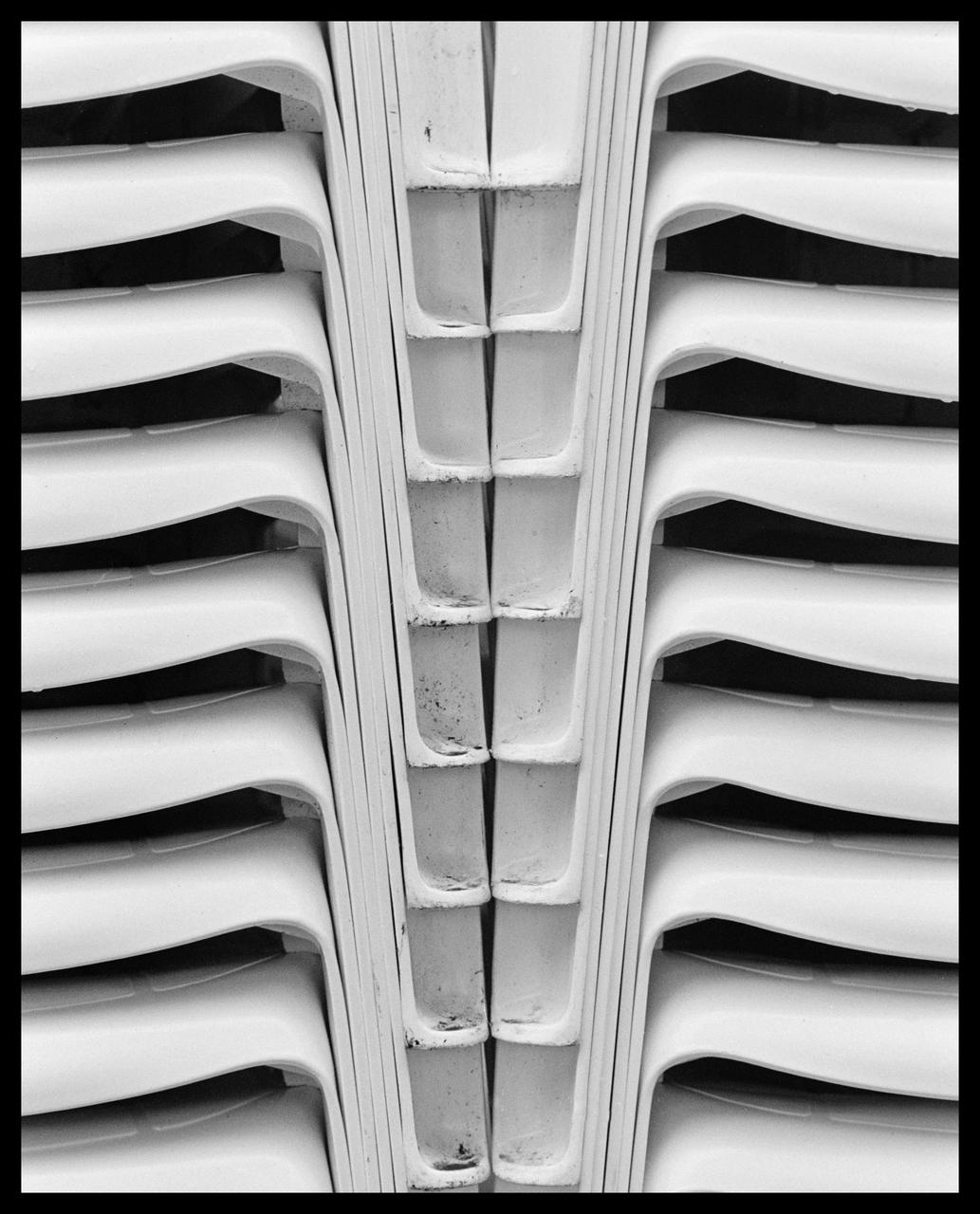 A somewhat abstract black-and-white photograph of two stacks of white plastic chairs standing side by side, creating a vertical symmetry.

Camera: Nikon F2SB
Lens: Nikkor-S.C Auto 55mm f/1.2
Film: Ilford HP5 Plus