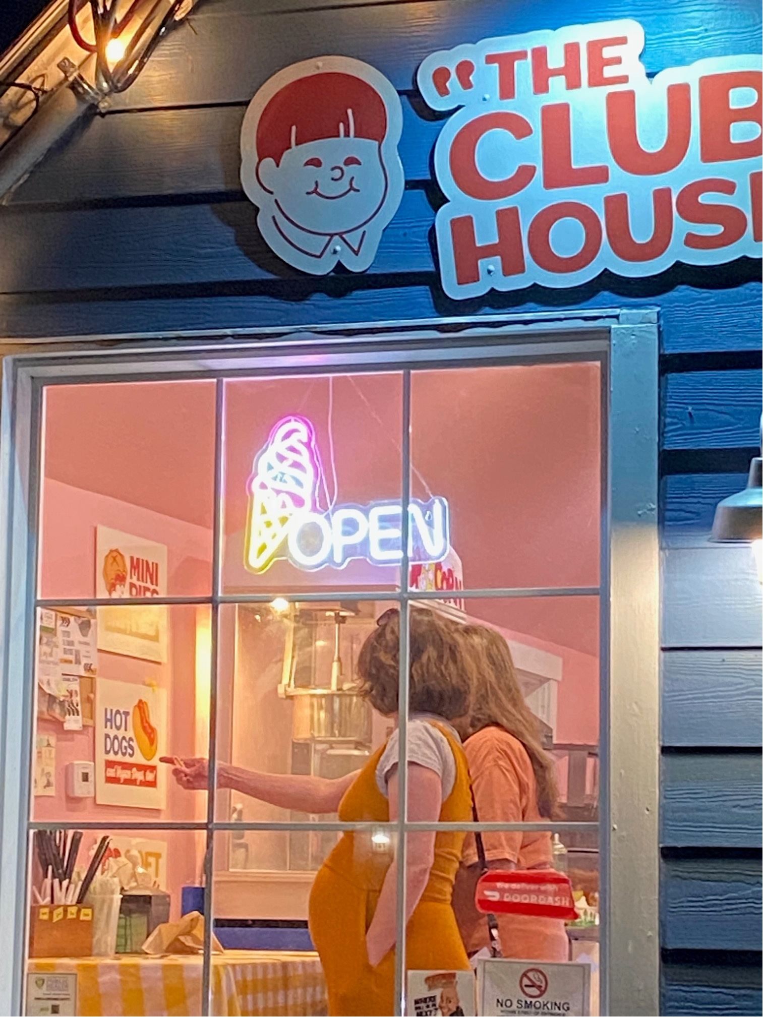 Color image of two customers in an ice cream shop in Indianapolis, Indiana, USA. Image shows two customers, one an expectant mother, selecting their ice cream confections inside the store, visible through a window with a OPEN neon sign in the window showing an ice cream cone. The shop is painted blue and reads "The Club House" on the wall.