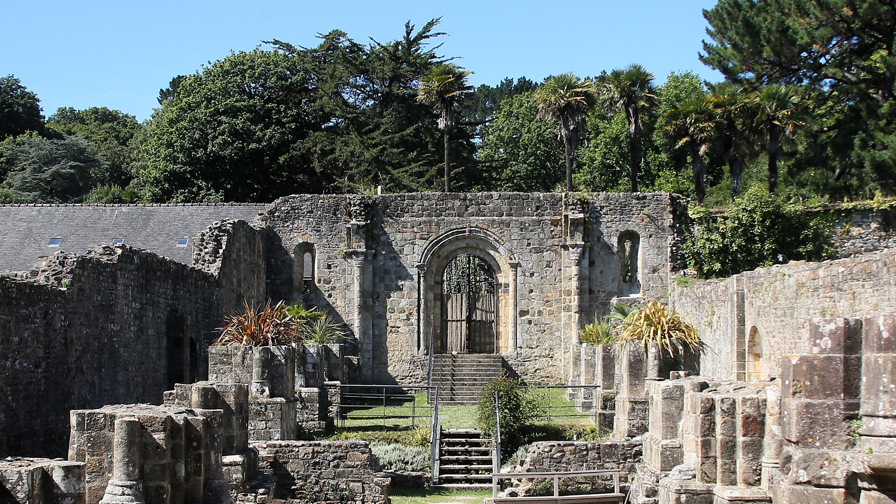View inside a derelict, medieval abbey. There are columns of about head height, and external walls considerably higher. There are trees in the background.
