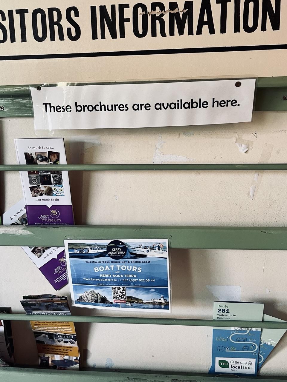 A mostly empty display case at a Visitors Information kiosk has a sign that reads: “These brochures are available here.”