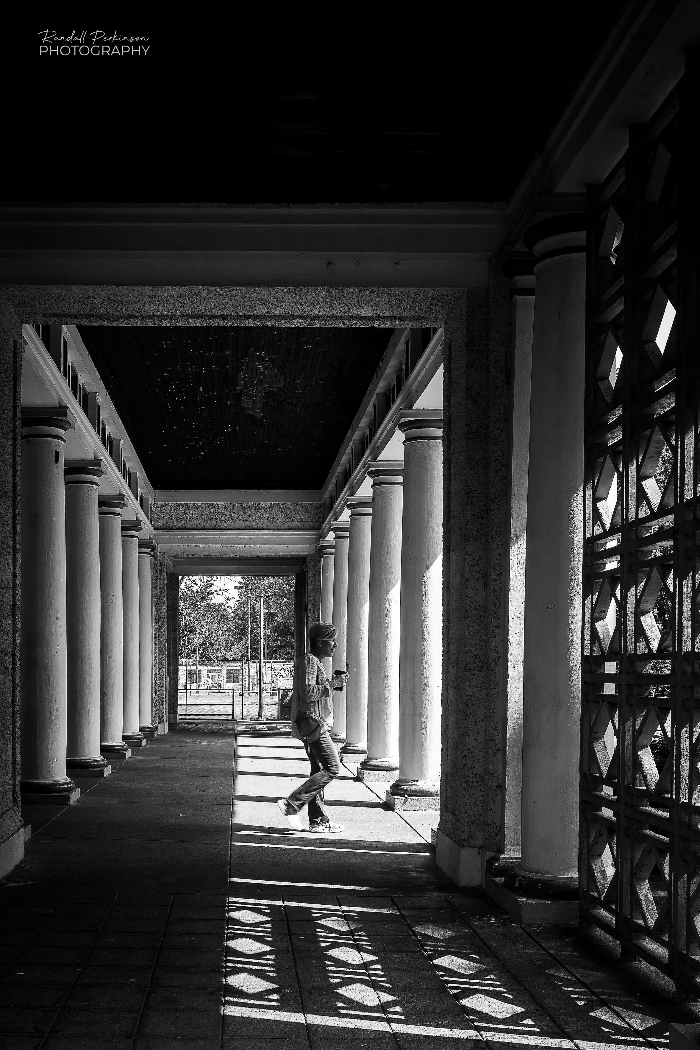 A women walks through a park building with multiple roman columns.