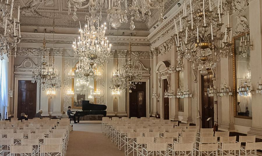 Una sala muy elegante llena de sillas vacías y al fondo un pianista
