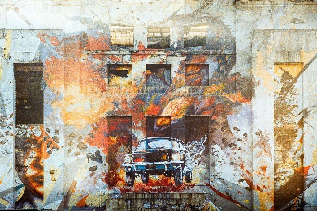 graffiti of car crashing out of a burning building, painted into a white wall