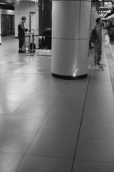 Ilford Delta 3200 (FF)

English
A black and white photograph of the inside of an underground station. Some people are standing at the side of the platform which have marble columns. Behind the columns, a worker with a helmet, seems to be working on something.

中文
一张黑白照片.照片中是地铁站的内部.站台上站了一些人,背靠大理石的立柱.立柱后面是一个戴着头盔的工人似乎在作业.