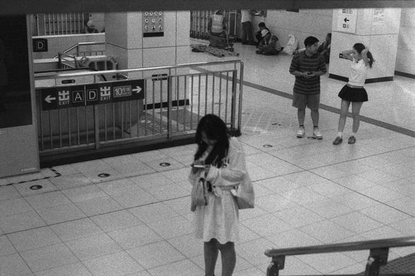 Ilford Delta 3200 (FF)

English
A black and white photograph of the inside of an underground station. Some people are walking in the station hall. Some other people behind them are sitting on the mound by the side of the column which has sign attached to it. There is a staircase coming from the level beneath. Metal rails are on the side of the entrance of the staircase with direction signs attached to it.

中文
一张黑白照片.照片中是一个地铁站的内部.一些人在走动,另一些人坐在后面靠墙的位置.旁边是一个立柱,上面有标志牌.有一个通向下层的台阶.台阶的出入口旁是金属的扶手,上面有方向…