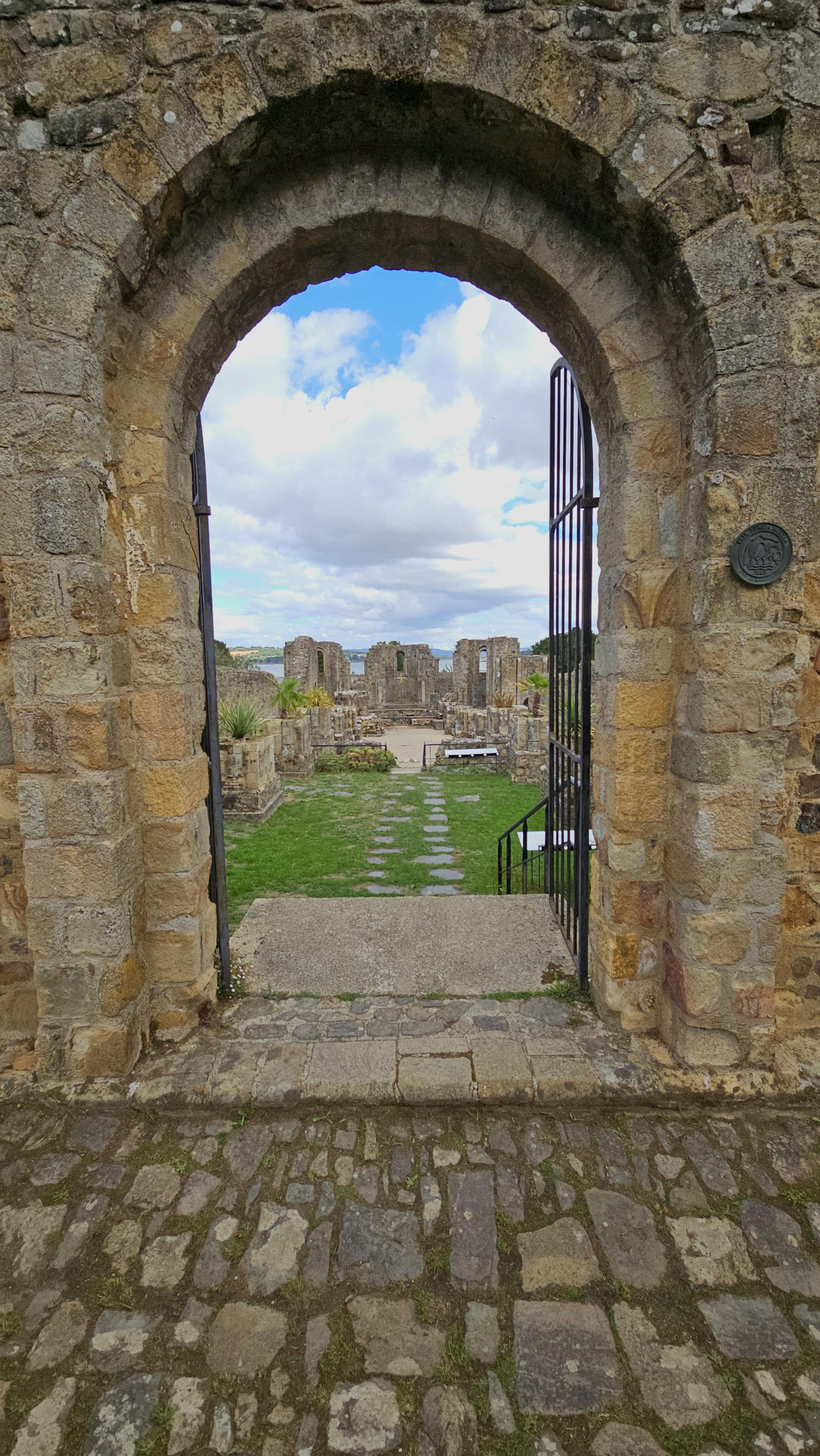 View through a door in a stone wall, onto a ruined church.