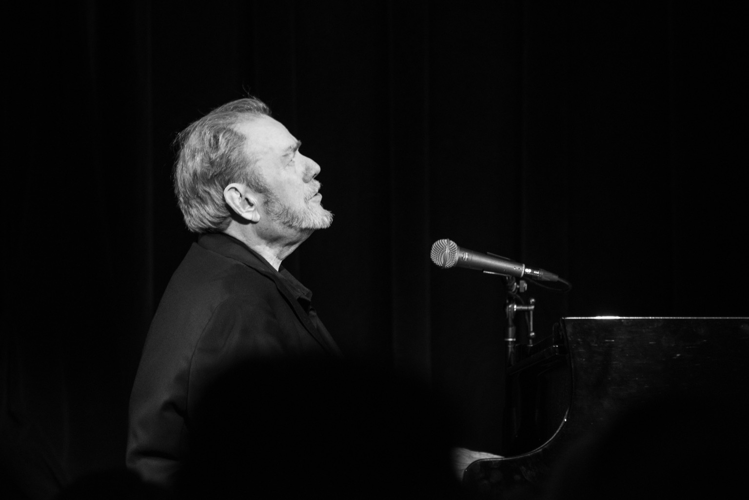 Jimmy Webb, head facing sjyward, sings at the grand piano.