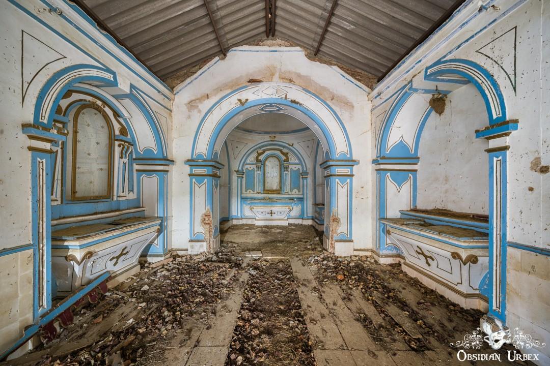 An abandoned chapel interior featuring ornate blue and white arches, a debris-covered floor, and a distant altar