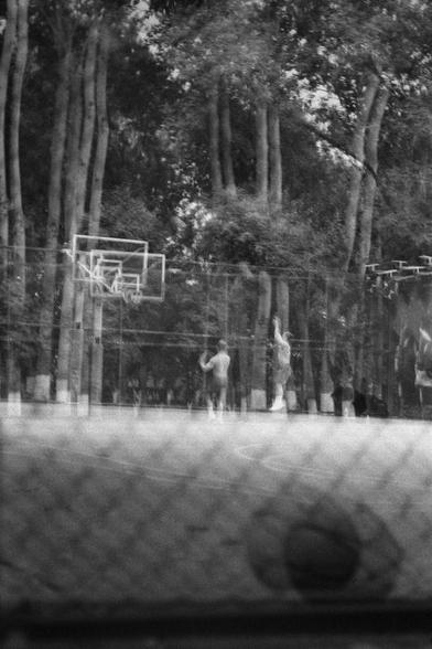 Ilford HP5 Plus 400 (FF)

English
A black and white photograph. A double exposure of a basketball court through safety net wires. A basket ball can be seen in the foreground while someone is shooting the hoop in the back.

中文
一张黑白照片.照片中是一个篮球场的双重曝光.前景中可以看到一个篮球在安全网的后面.背景中一个人在投篮.