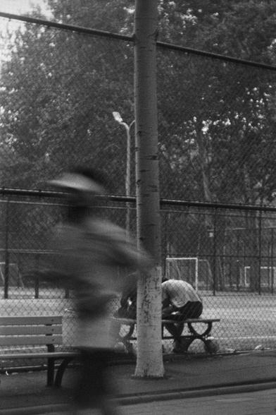 Ilford HP5 Plus 400 (FF)

English
A black and white photograph of a basketball court behind a safety net wire. A jogger can be seen in the foreground with a blurry figure. Someone else sits behind a tree on a bench. Many trees can be seen at the back.

中文
一张黑白照片.照片中有一个安全网后的篮球场.前景中有一个慢跑的人的模糊身影.后面在树后一个人坐在长凳上.背景中很多树.