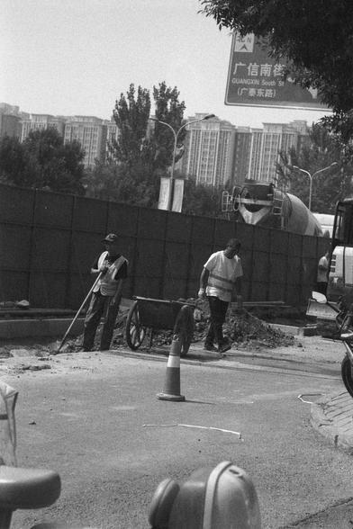 Ilford HP5 Plus 400 (FF)

English
A black and white photograph of a construction site on the street. Two workers are renovating the street surface. A traffic cone is in sight. An urban skyline is in the back.

中文
一张黑白照片.照片中是一个道路翻修的现场.两个工人正在工作.一个交通锥在路的中央.背景中是城市的天际线.