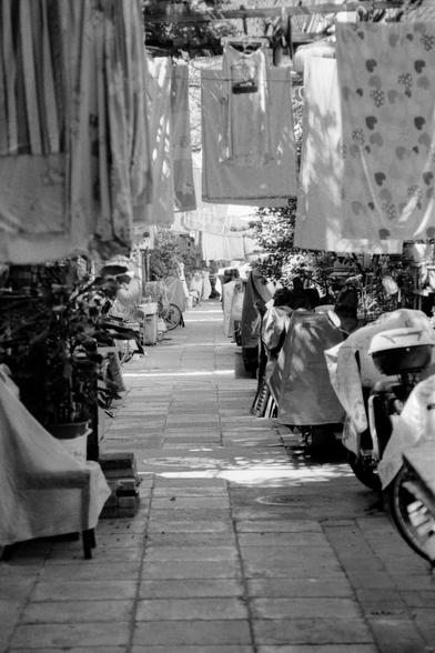 Lucky LUCKY SHD 400 (FF)

English
A black and white photograph of an alleyway. Many bicycles and motorcycles are parked on each side of the alleyway. Some bedsheets are hung on wires over the alleyway.

中文
一张小巷的黑白照片.小巷的两边停满了自行车和摩托车.小巷上方悬挂着很多被单.