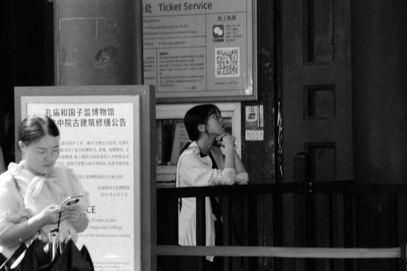 Lucky LUCKY SHD 400 (FF)

English
A black and white photograph. A girl is looking up, leaning against the barricade by the side of the ticket office of a tourist sight. A person stands by the side of an announcement.

中文
一张黑白照片.一个女孩开着上方沉思,靠着景点售票厅的栏杆.另一个人站在景区公告前.